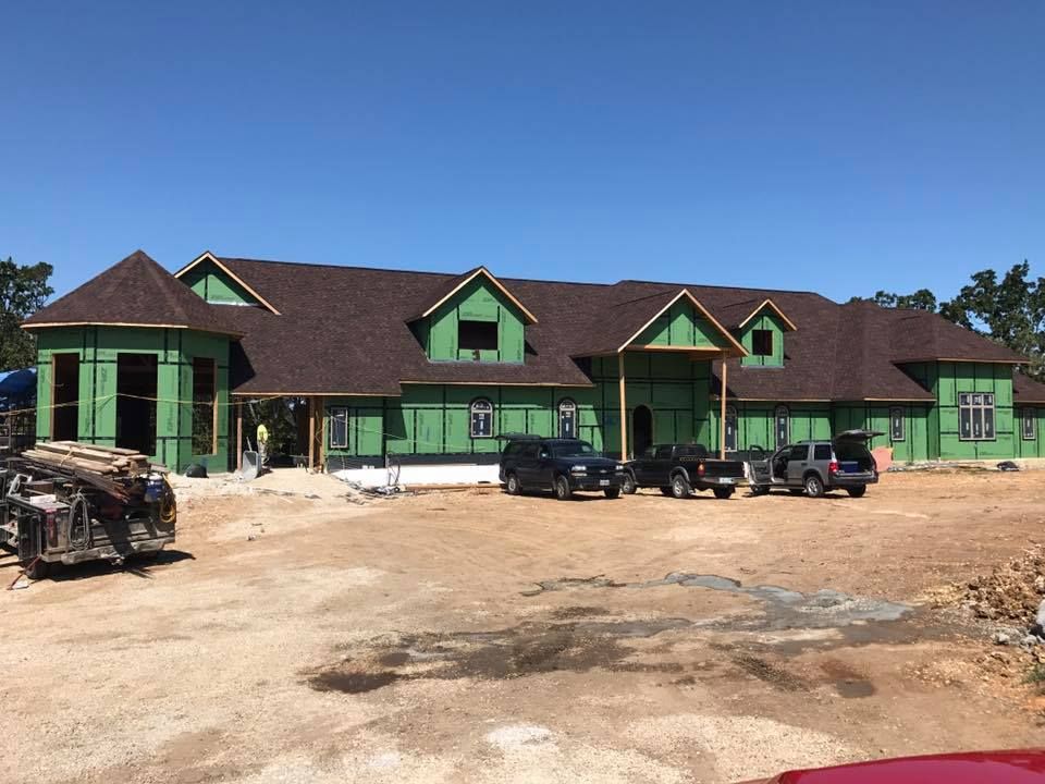 Green lodge-style building with multiple cars parked in front on a dirt lot under a clear blue sky