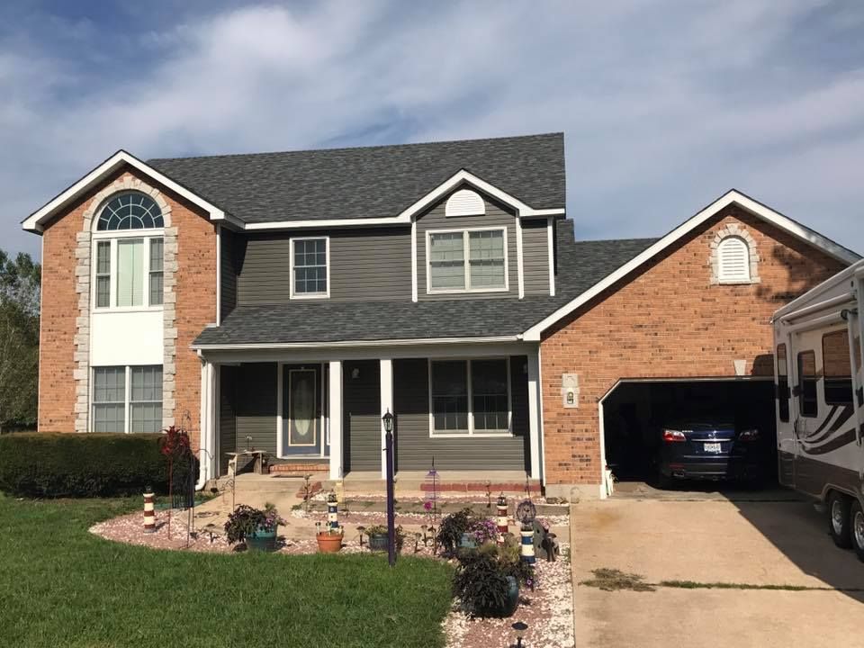 Two-story brick house with front porch, arched window, and attached carport under a cloudy sky