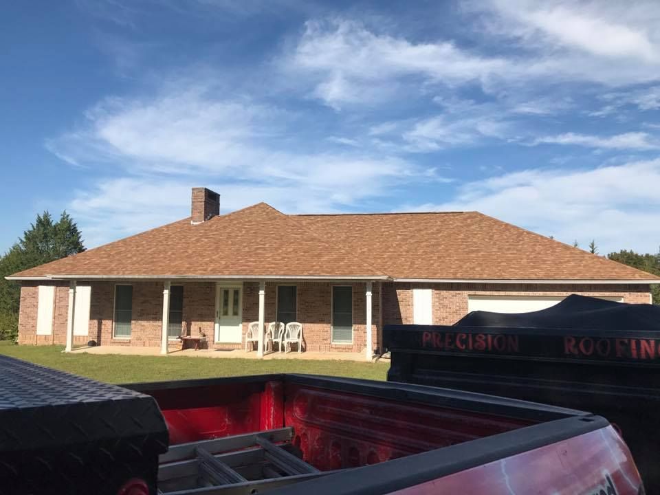 Single-story brick house with a red roof and white patio chairs under a blue sky