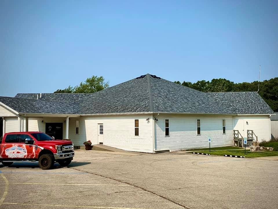 Single-story white building with dark roof and a red truck parked on a paved lot.