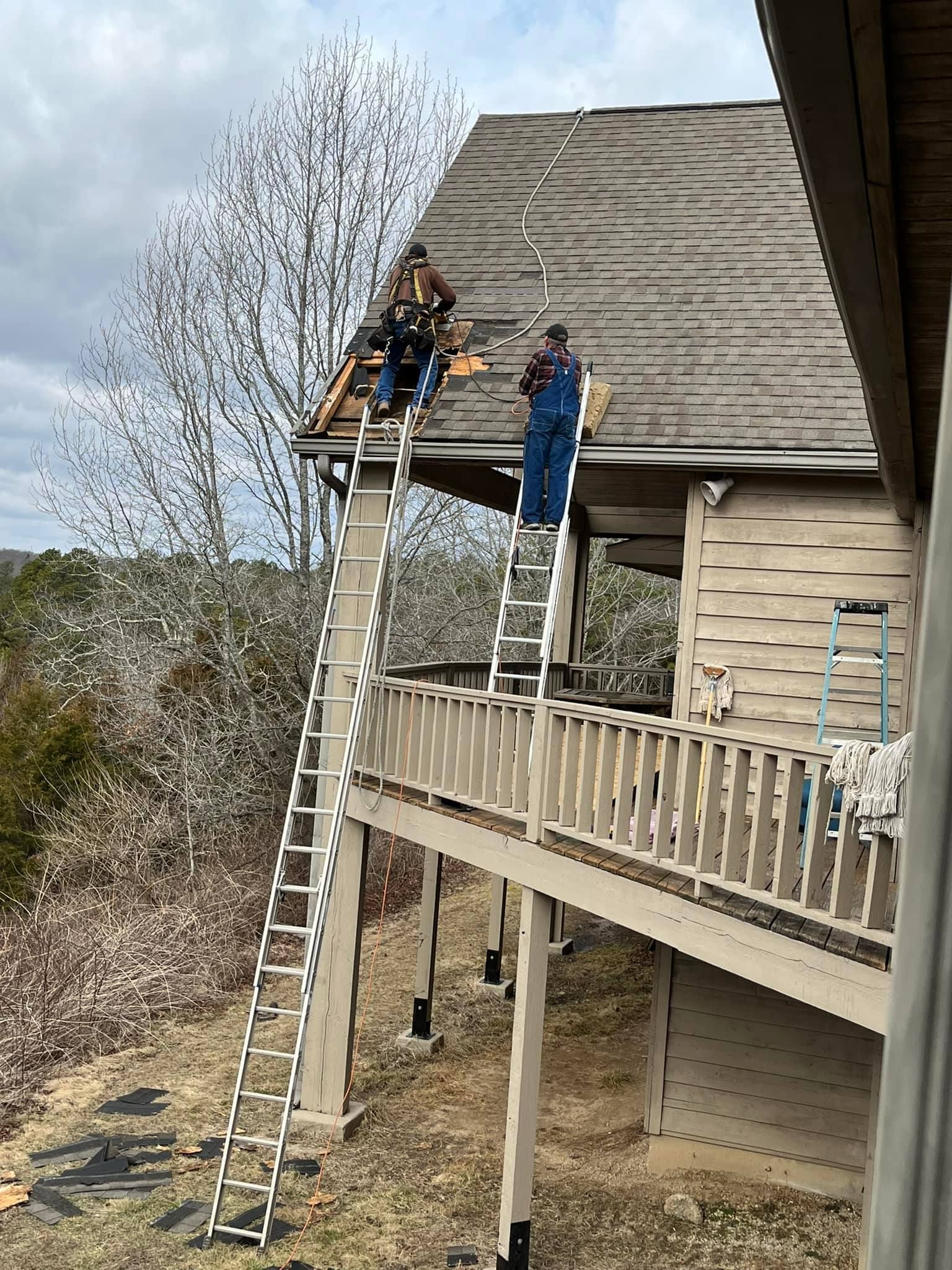 Two people on ladders repairing a roof beside a wooden house and porch