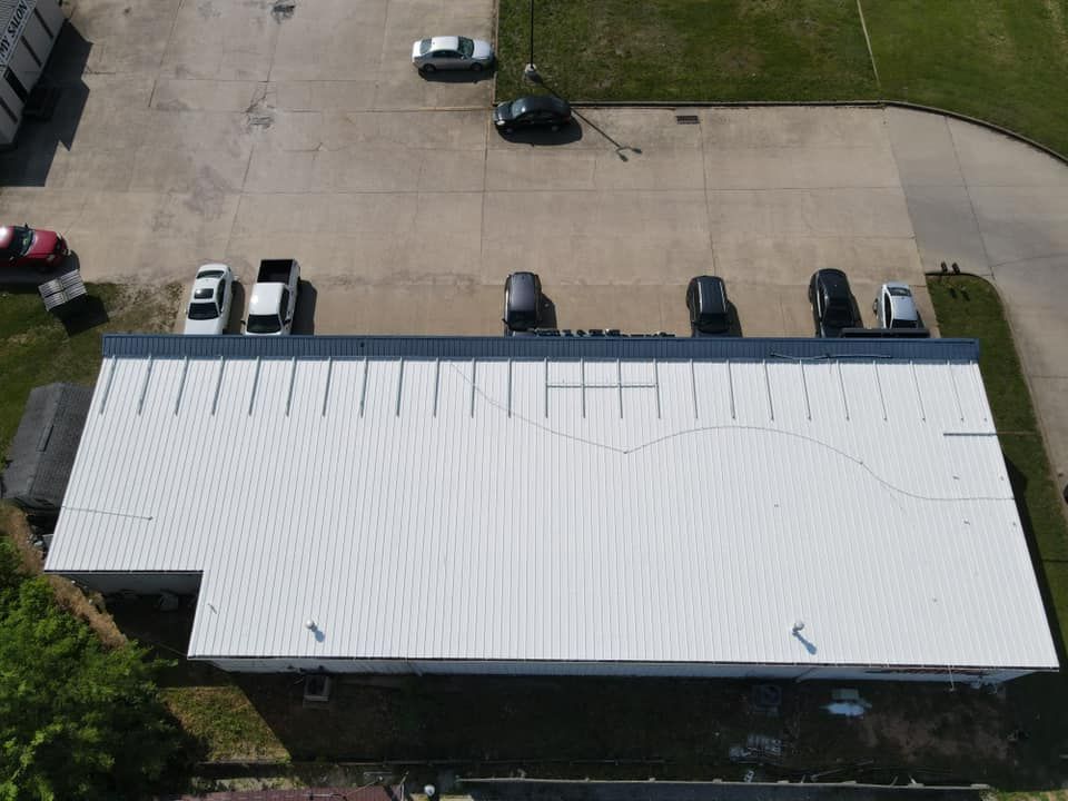 Aerial view of a white-roofed building beside a parking lot with several parked cars.
