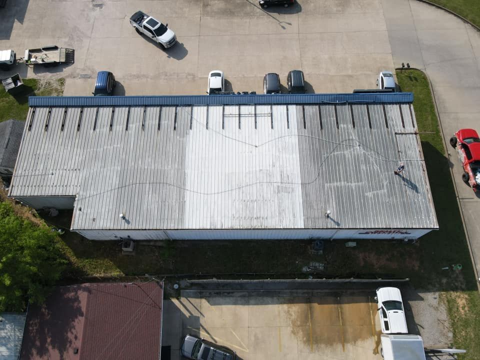 Aerial view of a long white-roofed building beside a parking lot with several cars and a road.