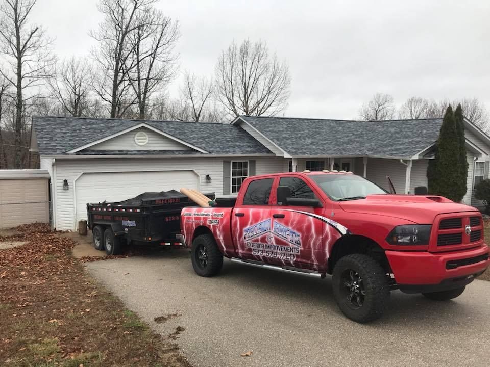 Red pickup truck towing a black trailer in a driveway in front of a house