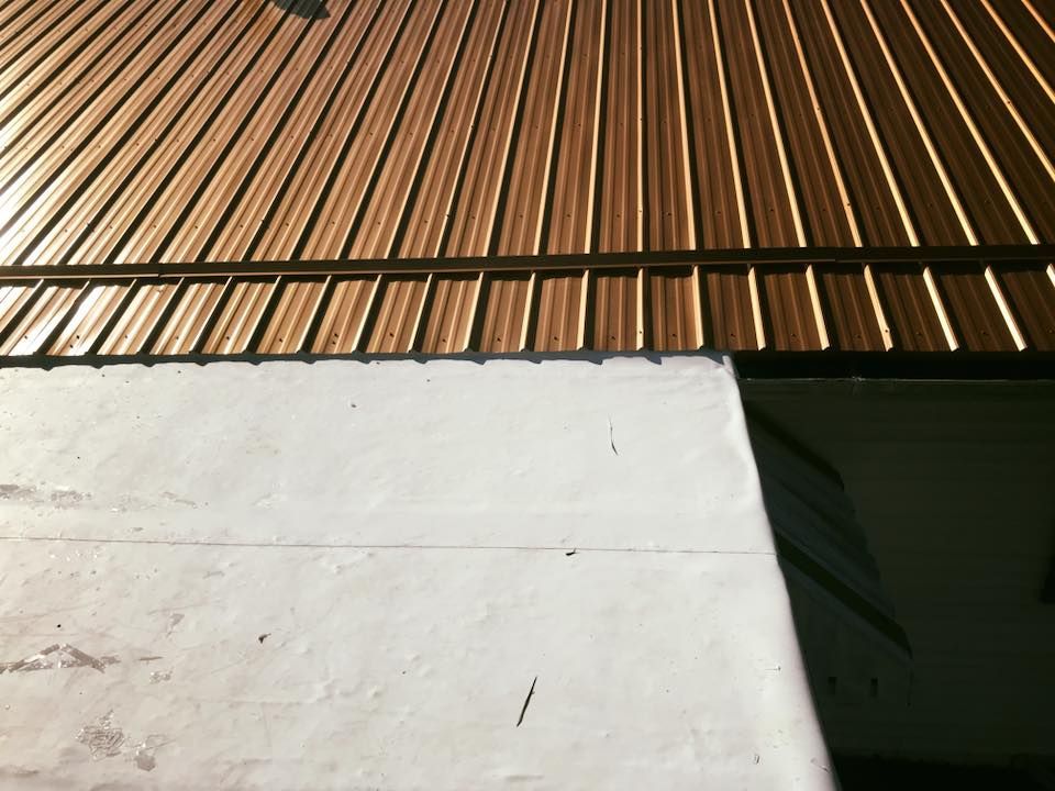 White wall beneath a copper corrugated roof with a dark green doorway shadow
