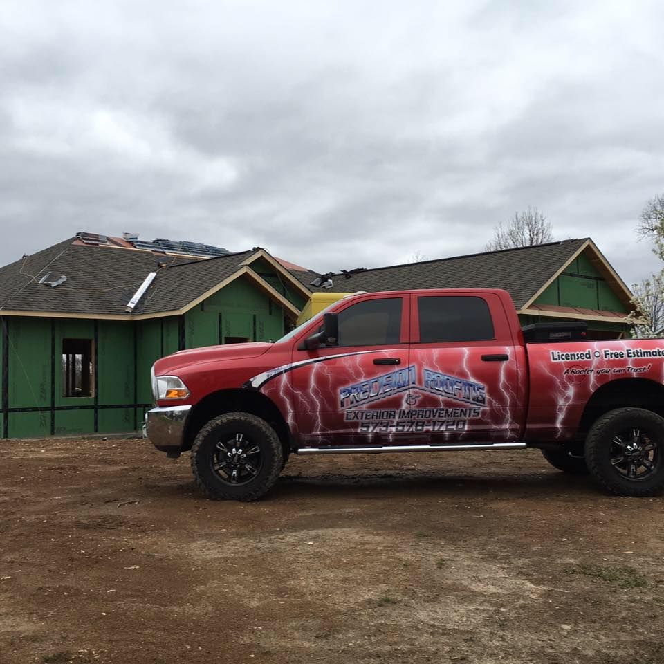 Red lifted pickup truck parked in front of green houses under a cloudy sky