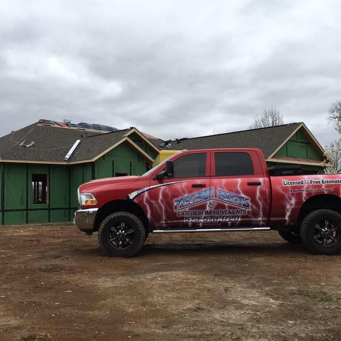 Red pickup truck parked in front of green houses under a cloudy sky