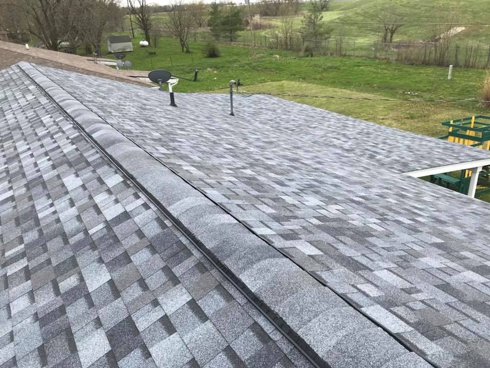 Gray shingled rooftop with vents overlooking a grassy yard and trees