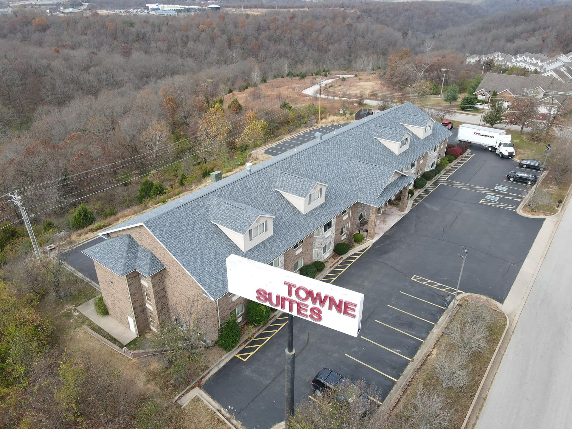 Aerial view of a Towne Suites hotel with parking lot and wooded surroundings.