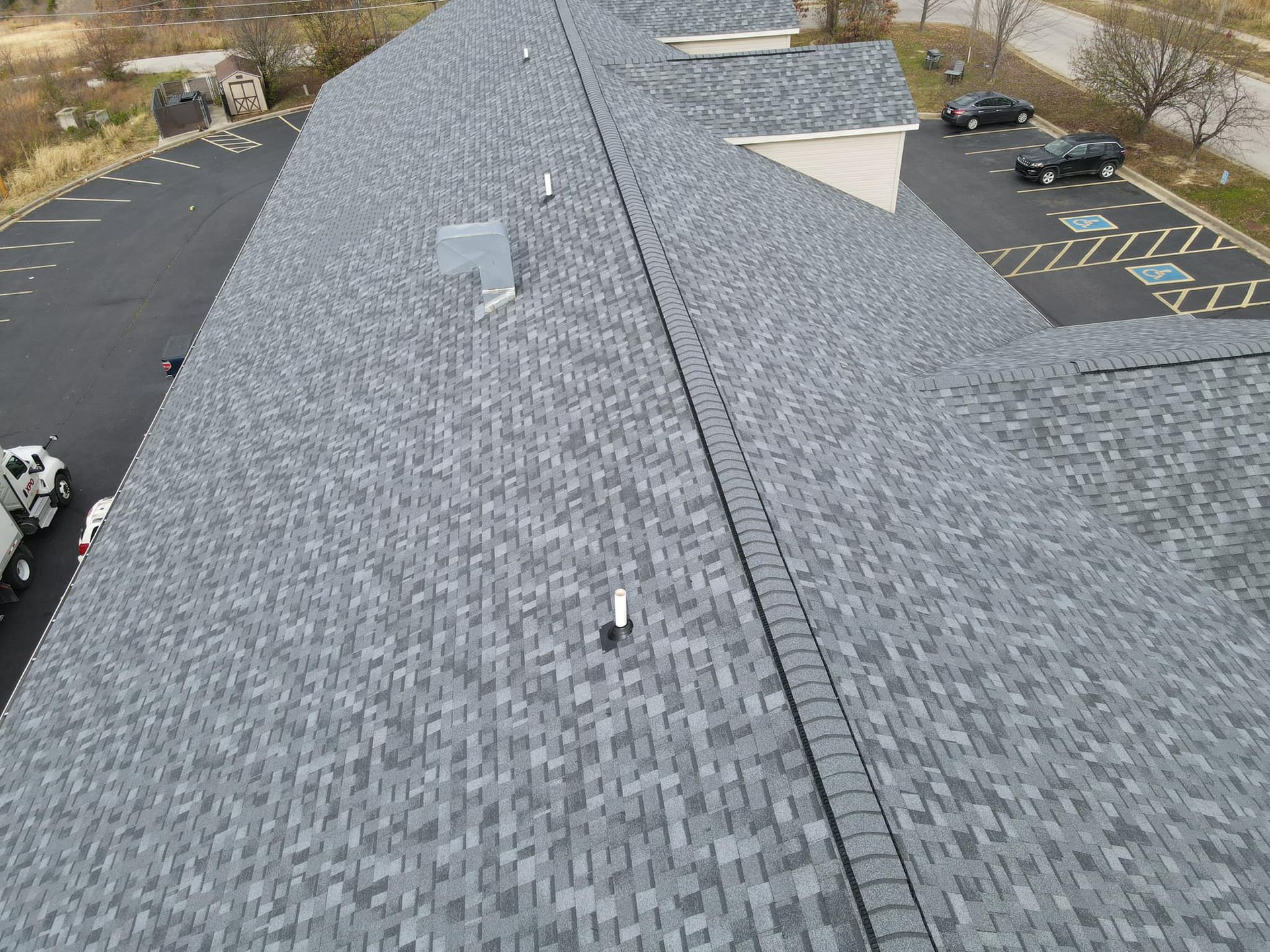 Aerial view of a gray shingled roof beside a parking lot with a few parked cars.