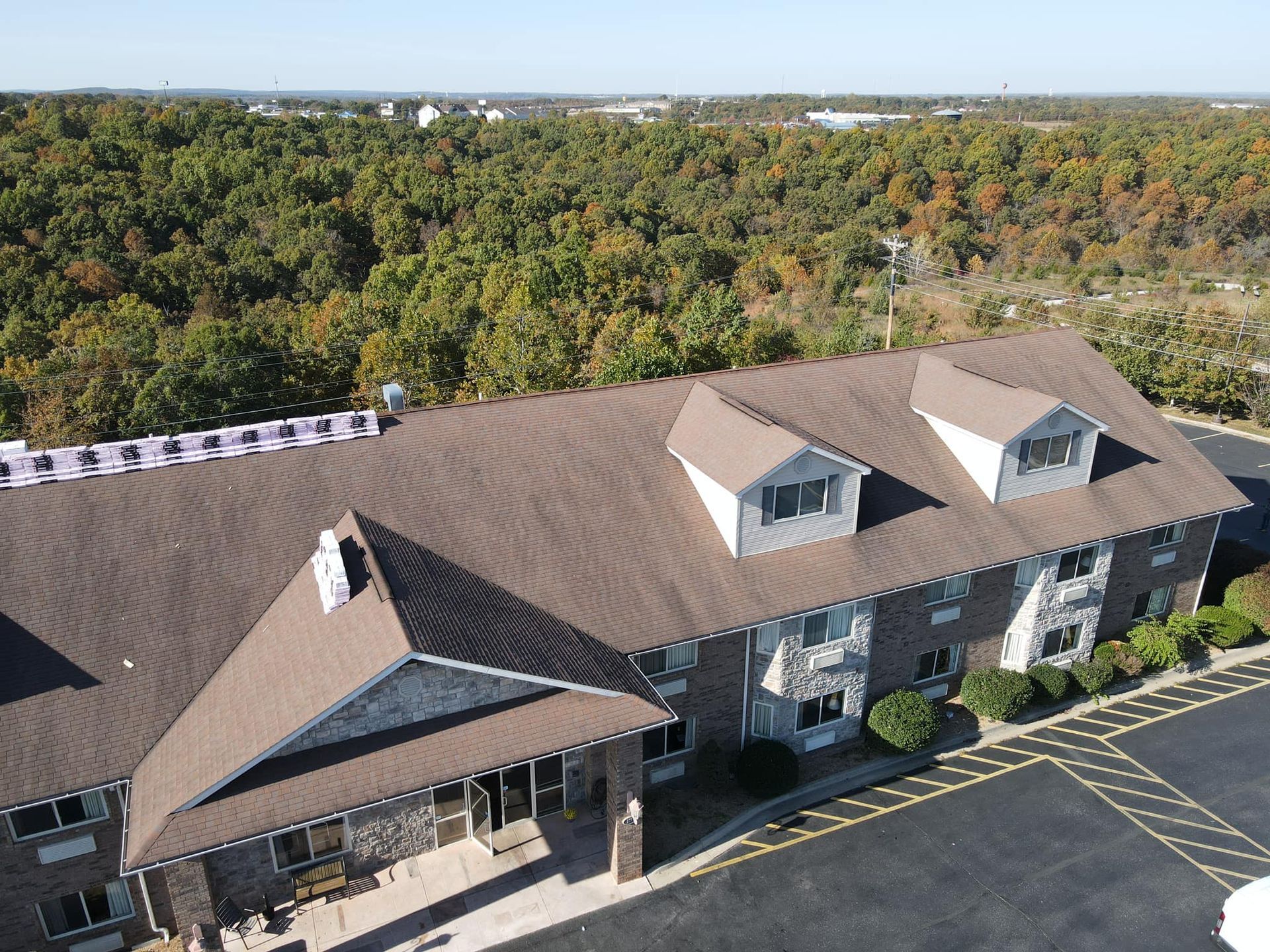 Aerial view of a brown-roofed office building beside a mostly empty parking lot and wooded area.