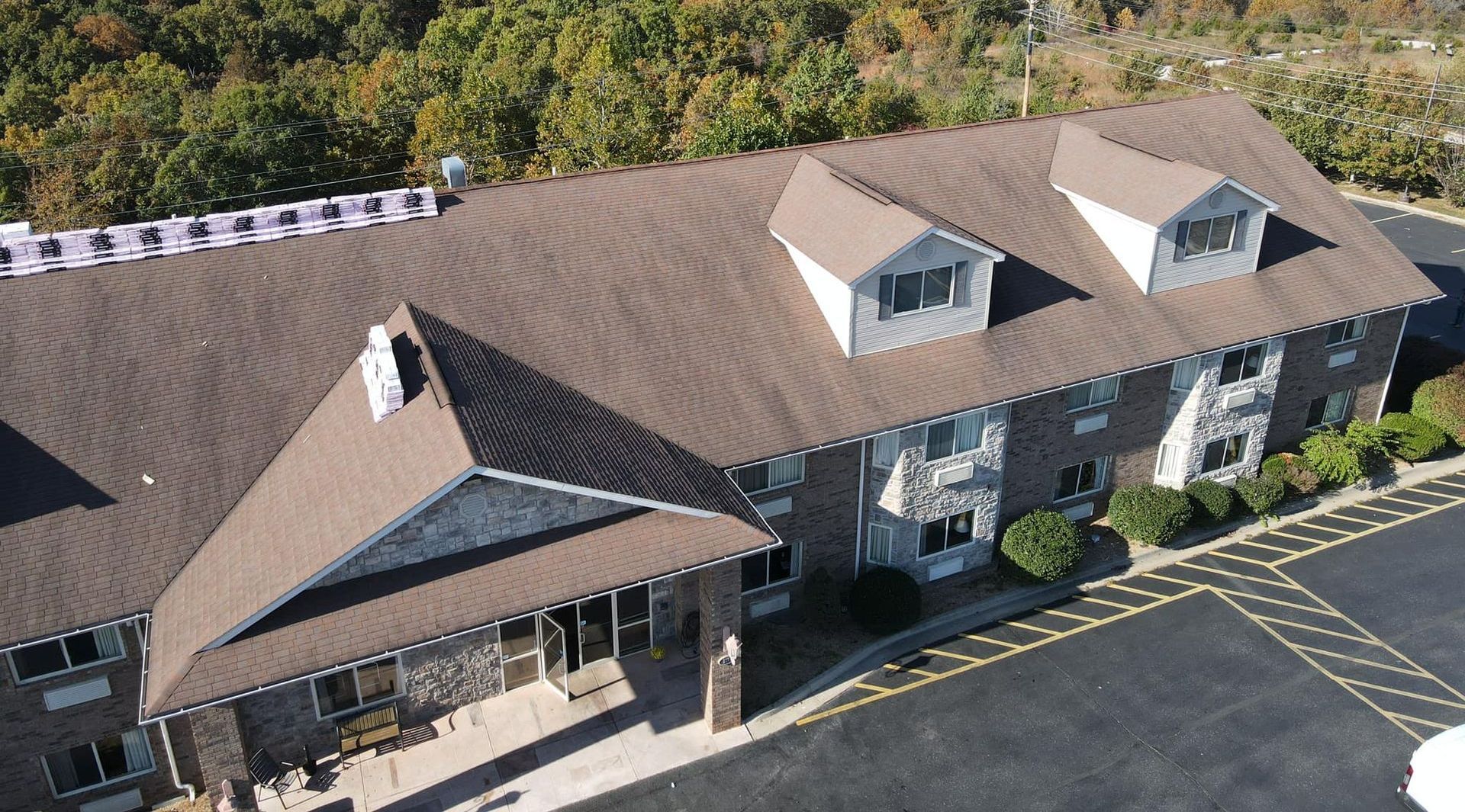 Aerial view of a tan-roofed building with dormer windows and a parking lot with yellow markings.