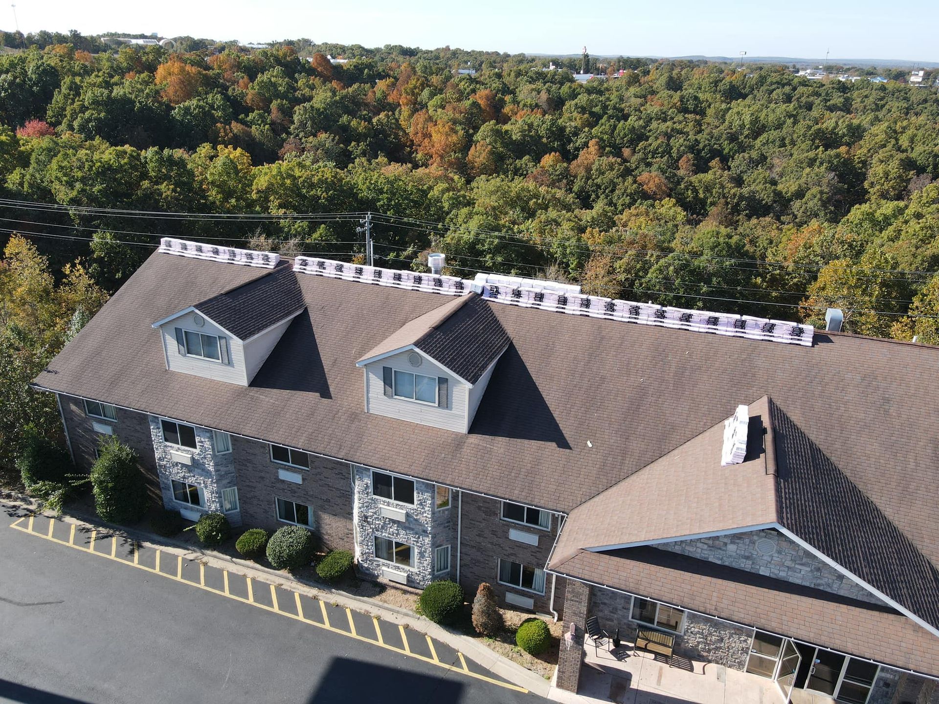 Aerial view of a brown-roofed building beside trees, with a forested backdrop.