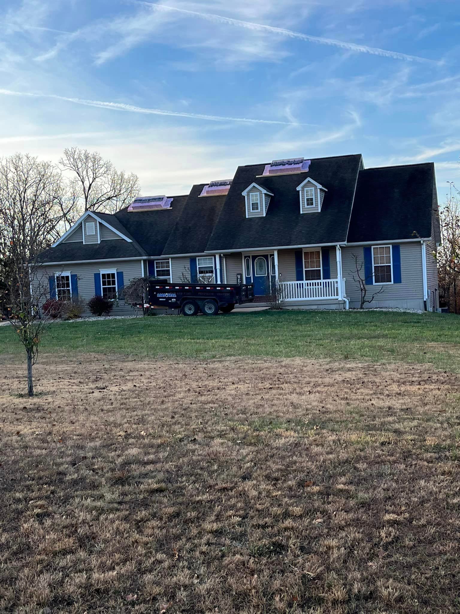 Large blue house with dormer windows, a black truck, and a white swing on a grassy yard under a cloudy sky