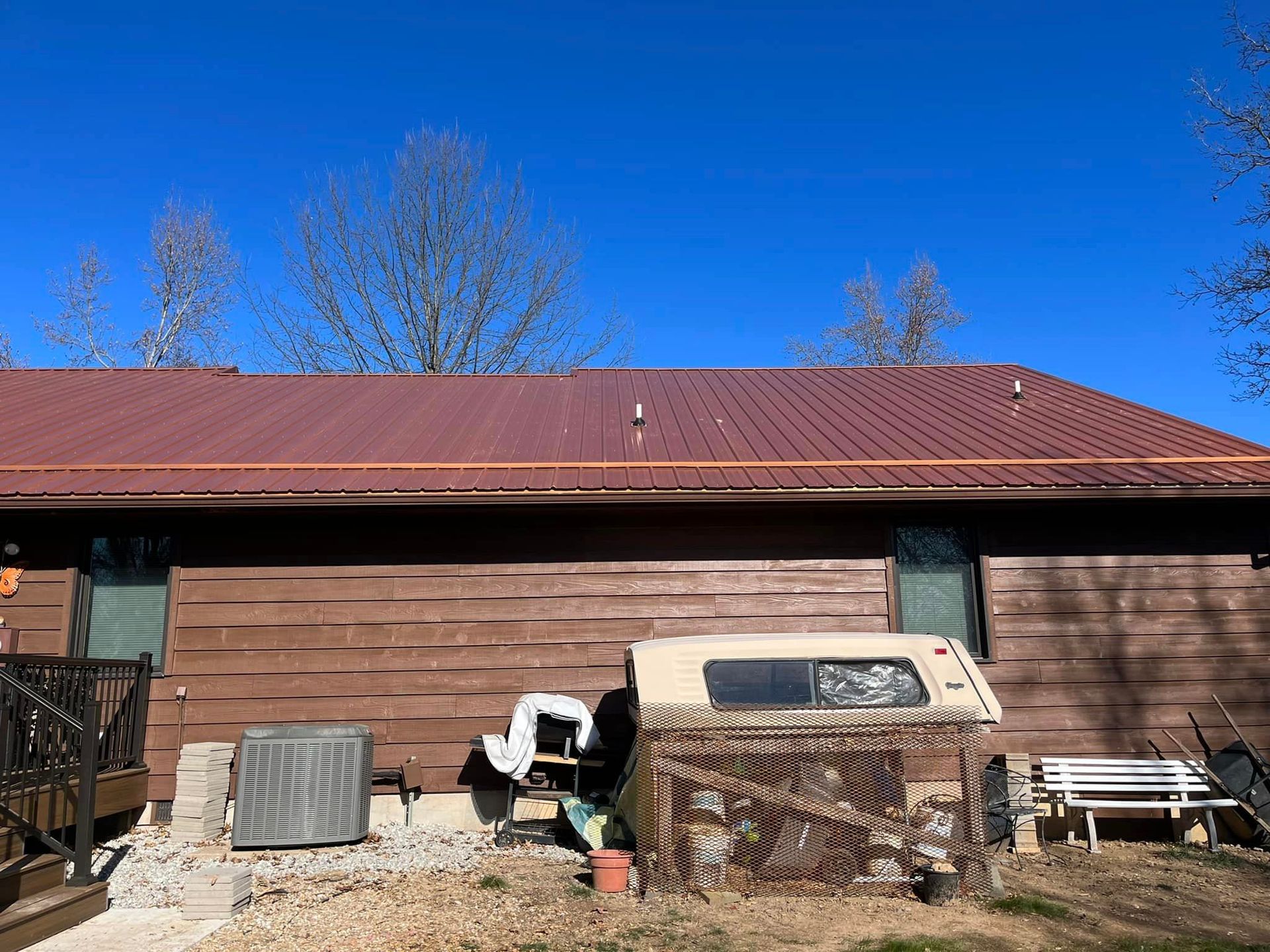 Backyard with a brown garage, red roof, clear blue sky, and scattered outdoor items in front