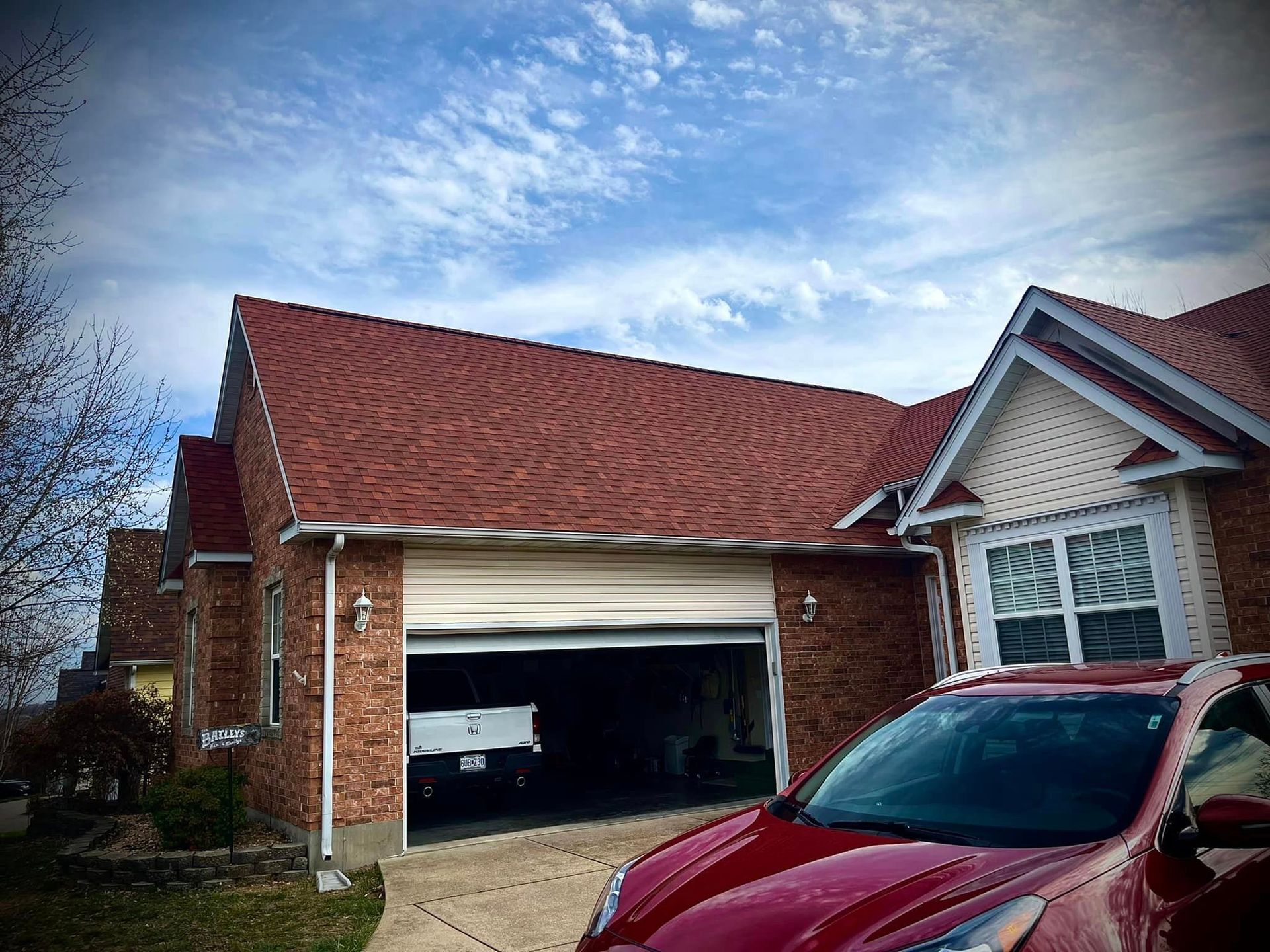 Brick house with red roof and open garage; red car parked in the driveway under a cloudy sky