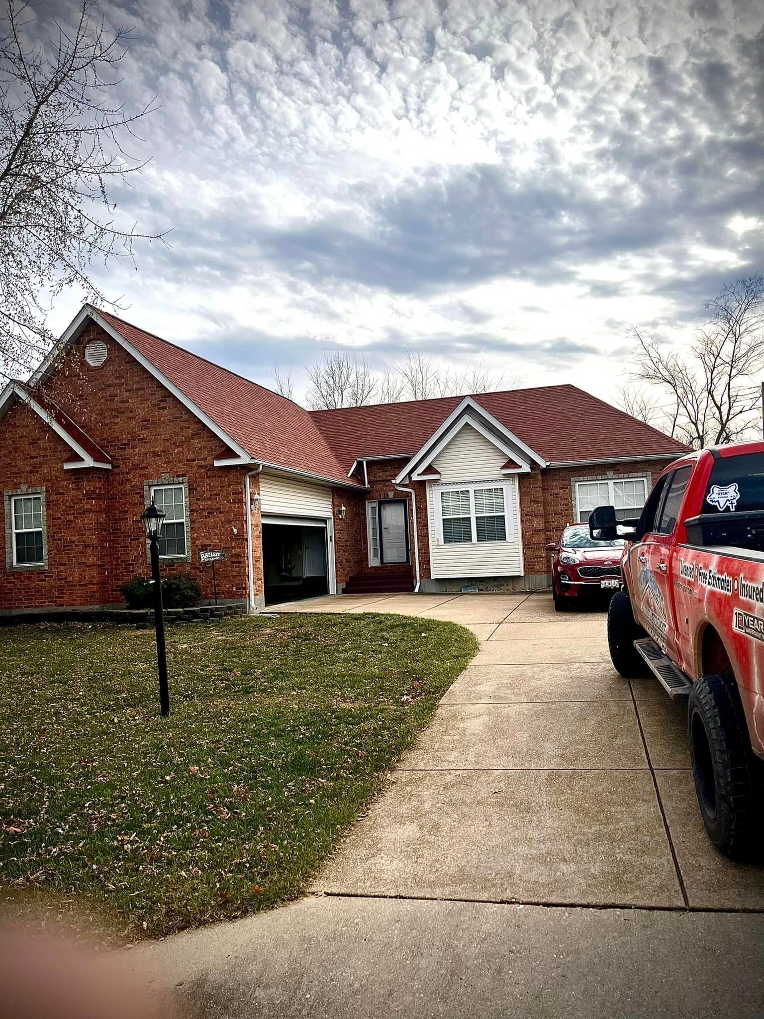 Suburban brick house with a driveway, parked red truck, and cloudy sky