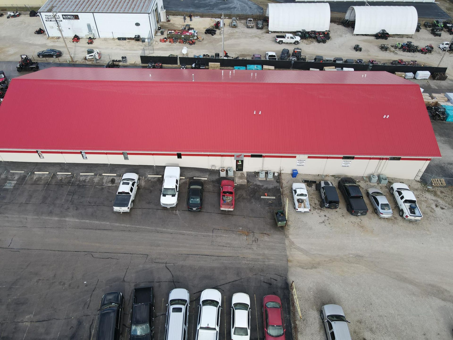 Aerial view of a red-roofed building with parked cars and trucks along its front lot.