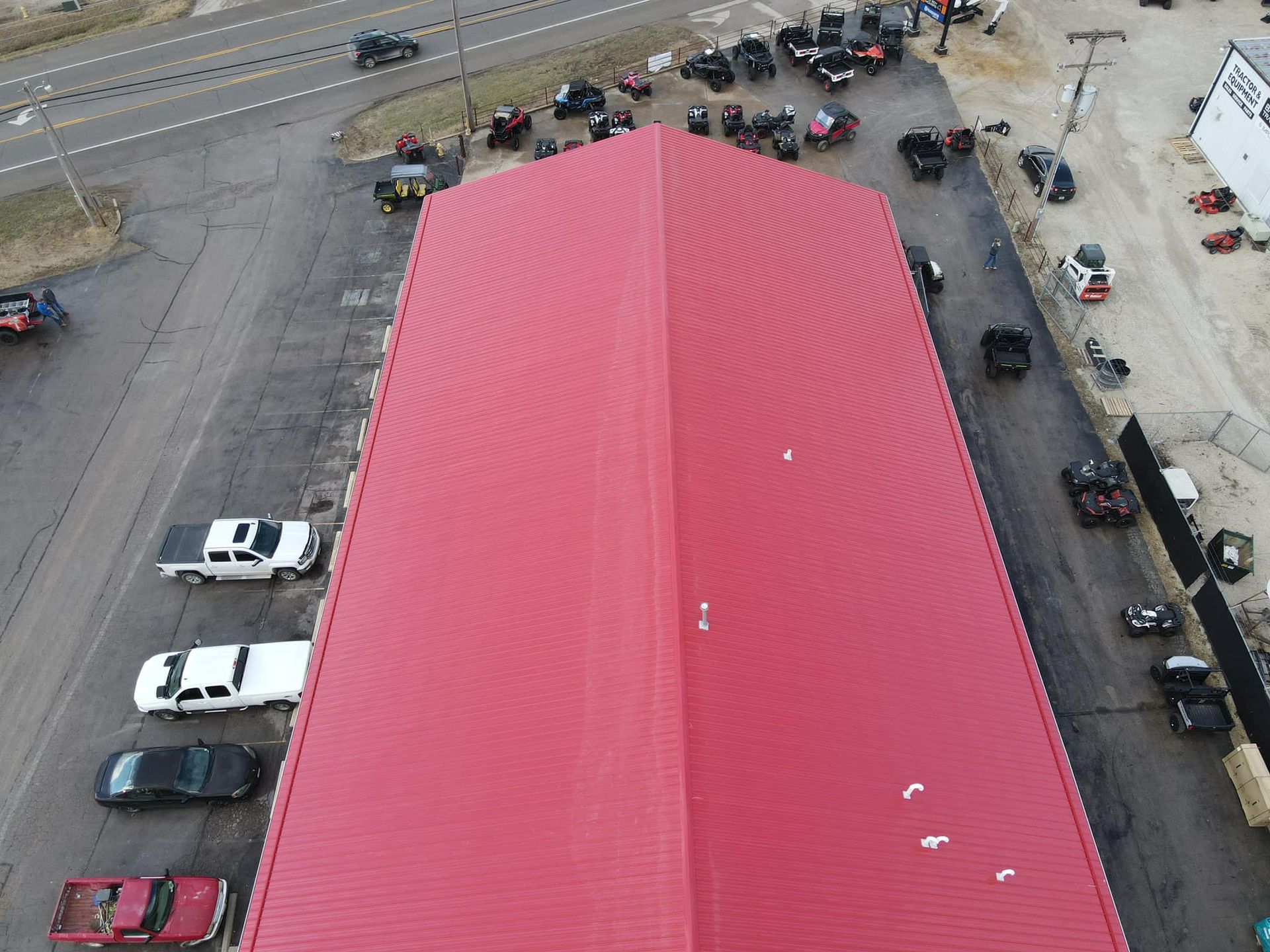 Aerial view of a red-roofed building with parked cars around it and a road nearby.