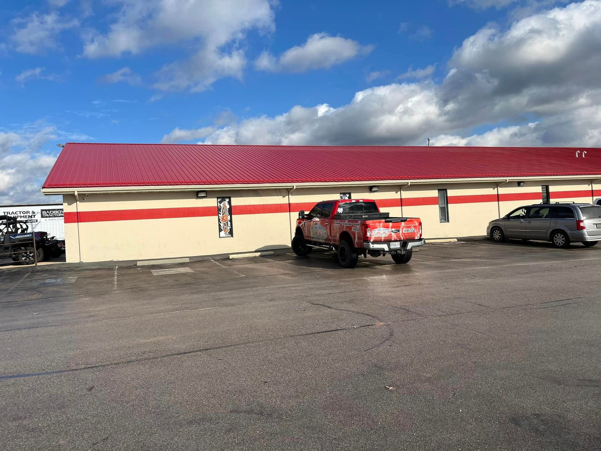 Red-roofed beige building with parked red SUV and gray car under a cloudy blue sky