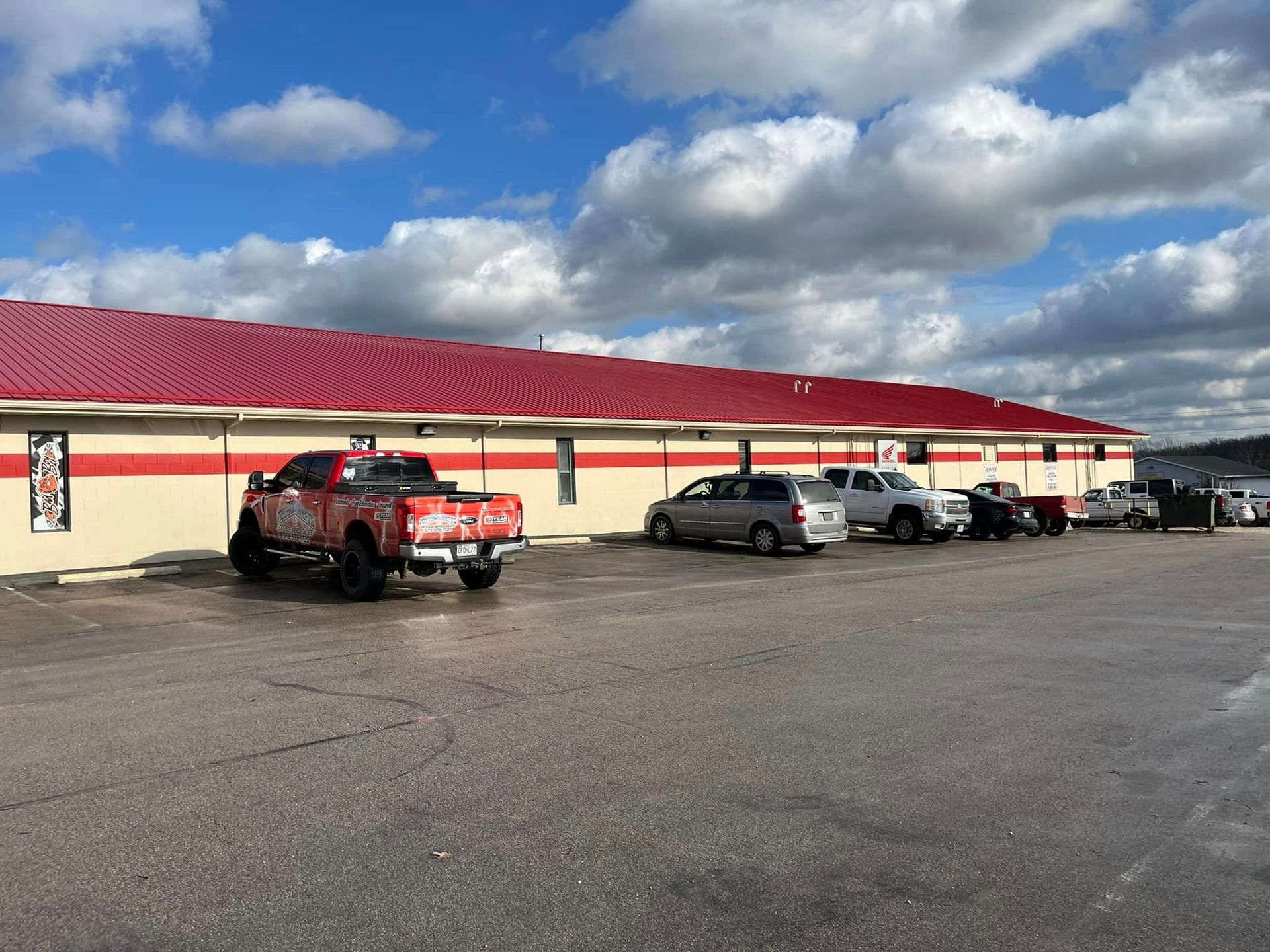 Red-roofed roadside building with parked cars under a cloudy blue sky