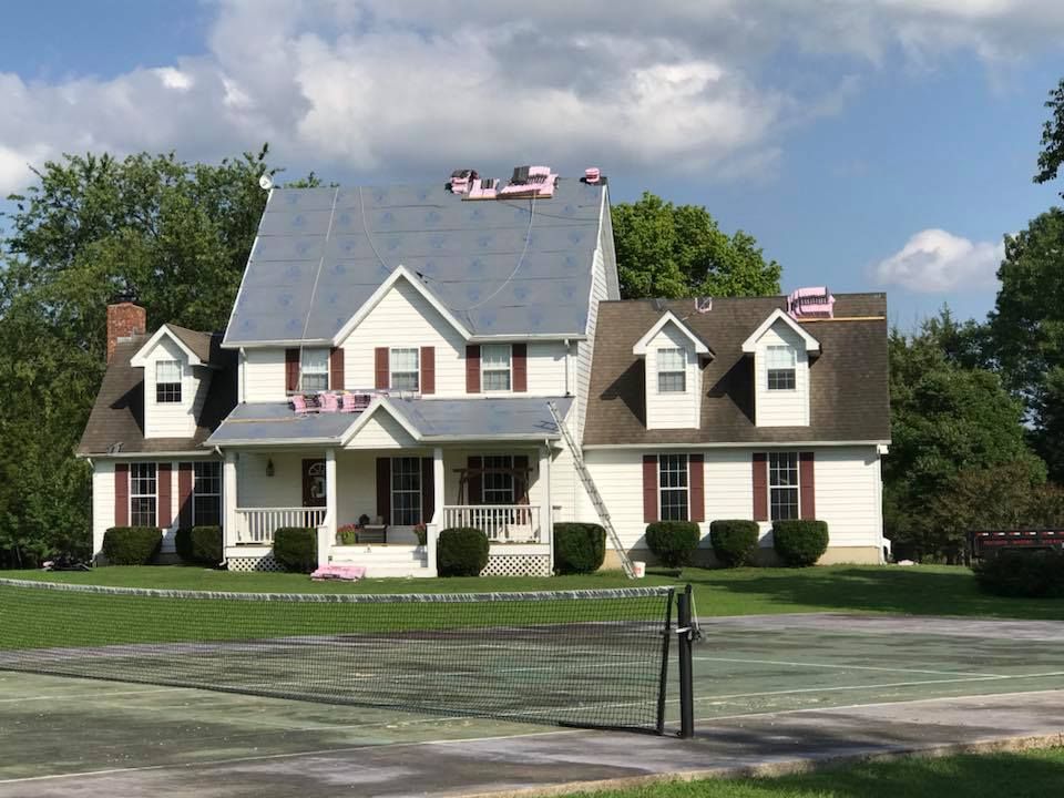 Large two-story suburban house with a gray roof, white porch, and manicured lawn under a blue sky