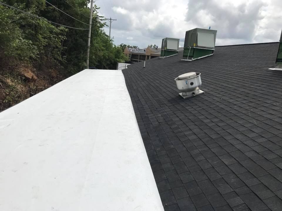 Flat rooftop with a white coated section, dark shingles, and HVAC units under cloudy skies.