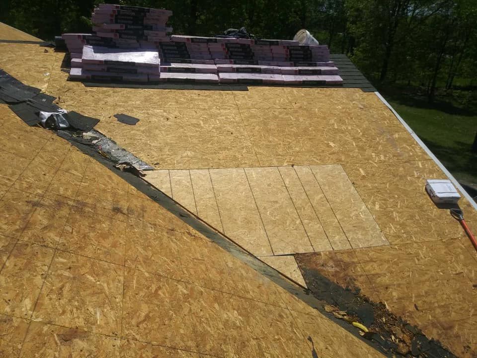Roof under construction with plywood sheathing, roofing materials stacked at the top, and a long seam down the slope