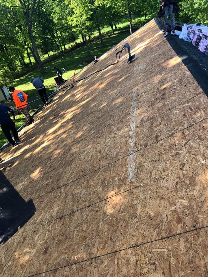 Workers installing plywood roofing on a sloped roof in a wooded area