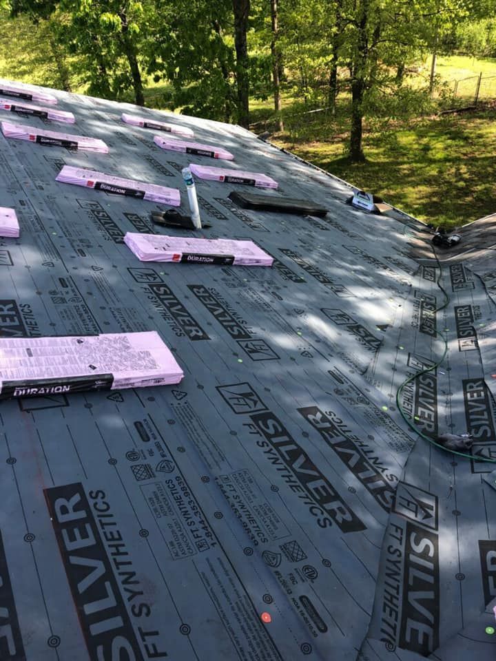 Roof underlayment being installed on a sloped roof, with pink insulation boards and trees in the background