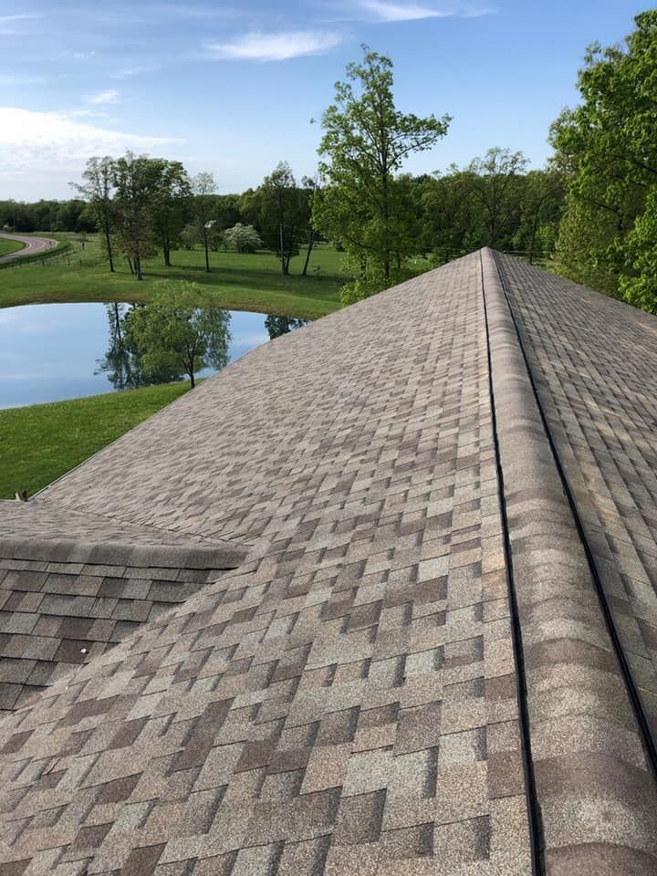 Shingled rooftop overlooking a pond, grassy park, and trees under a blue sky