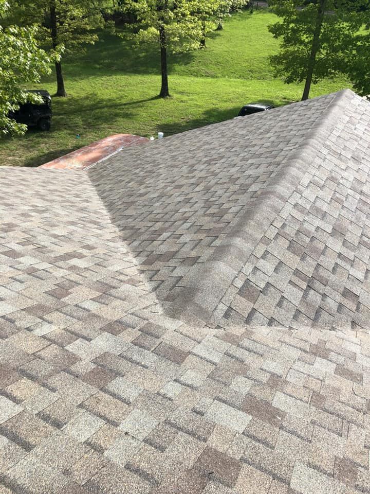 Shingled roof with a steep slope beside a grassy yard and trees