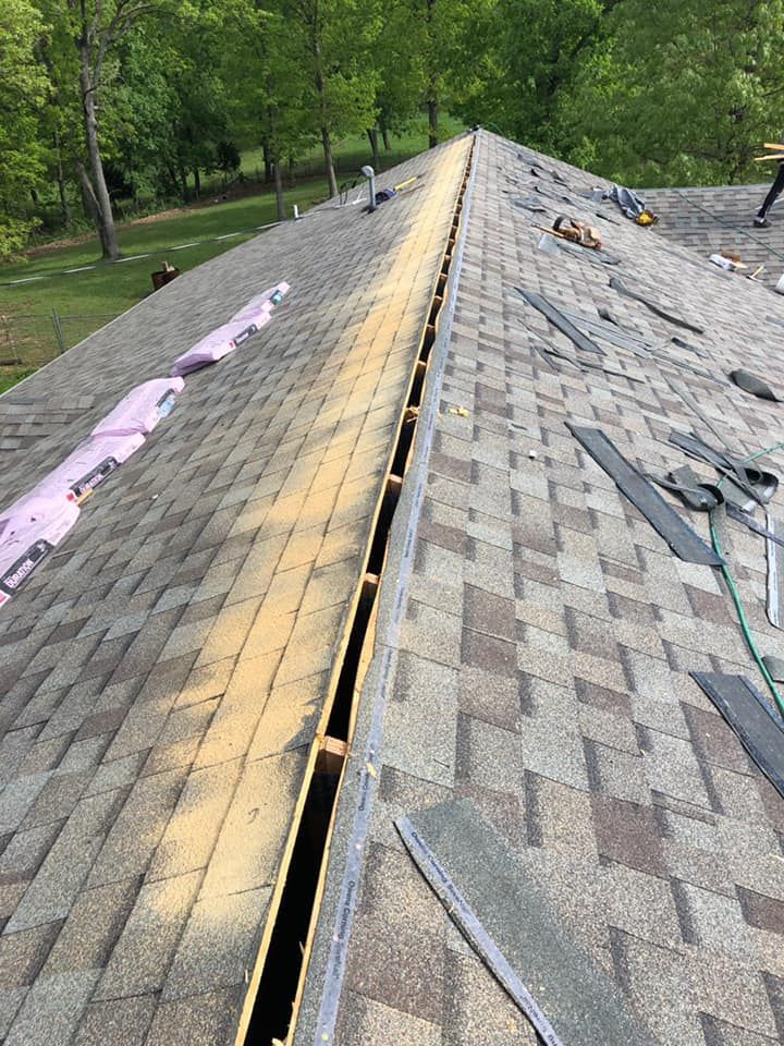Roofing shingles being replaced on a sloped house roof, with trees in the background.