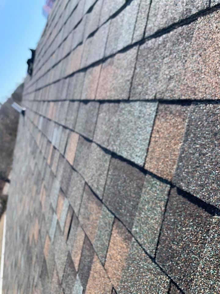 Close-up of a sloped roof with overlapping gray and brown shingles against blue sky