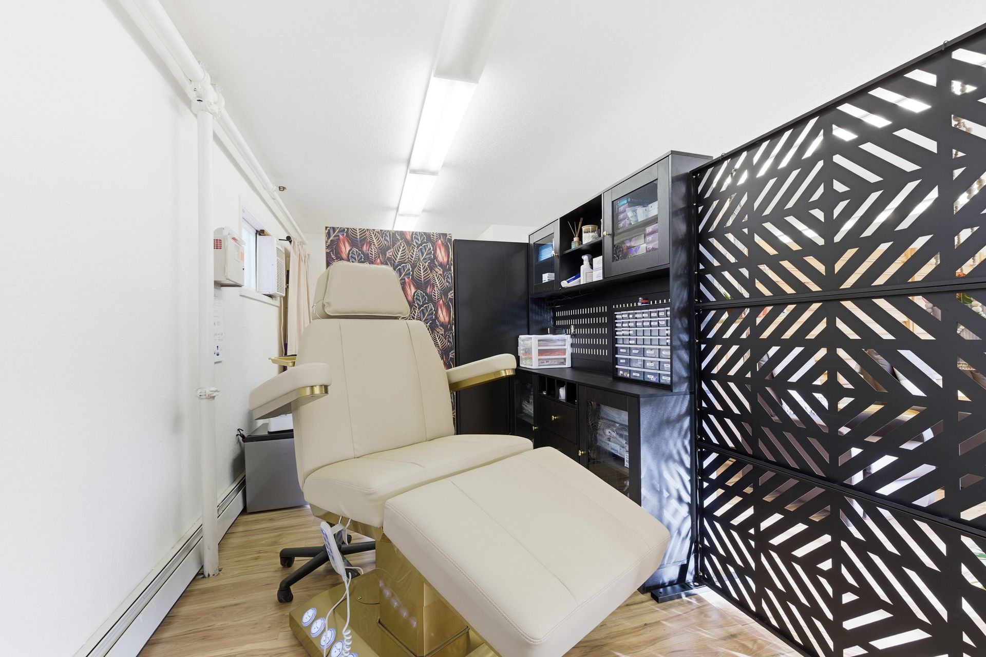Cream-colored treatment chair in a narrow salon or clinic room with black patterned storage cabinets.