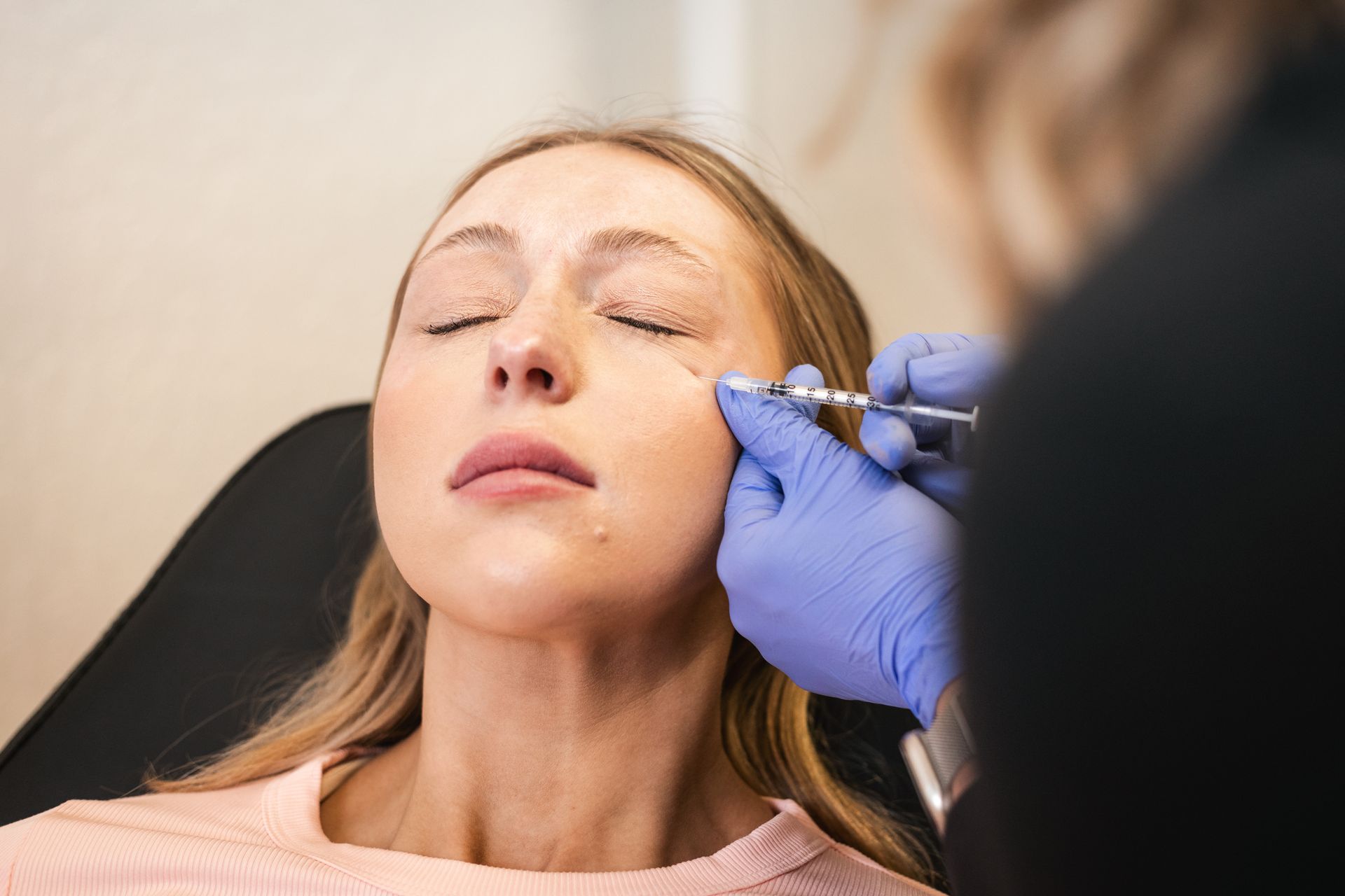 Woman receiving a cosmetic facial injection from a clinician wearing blue gloves
