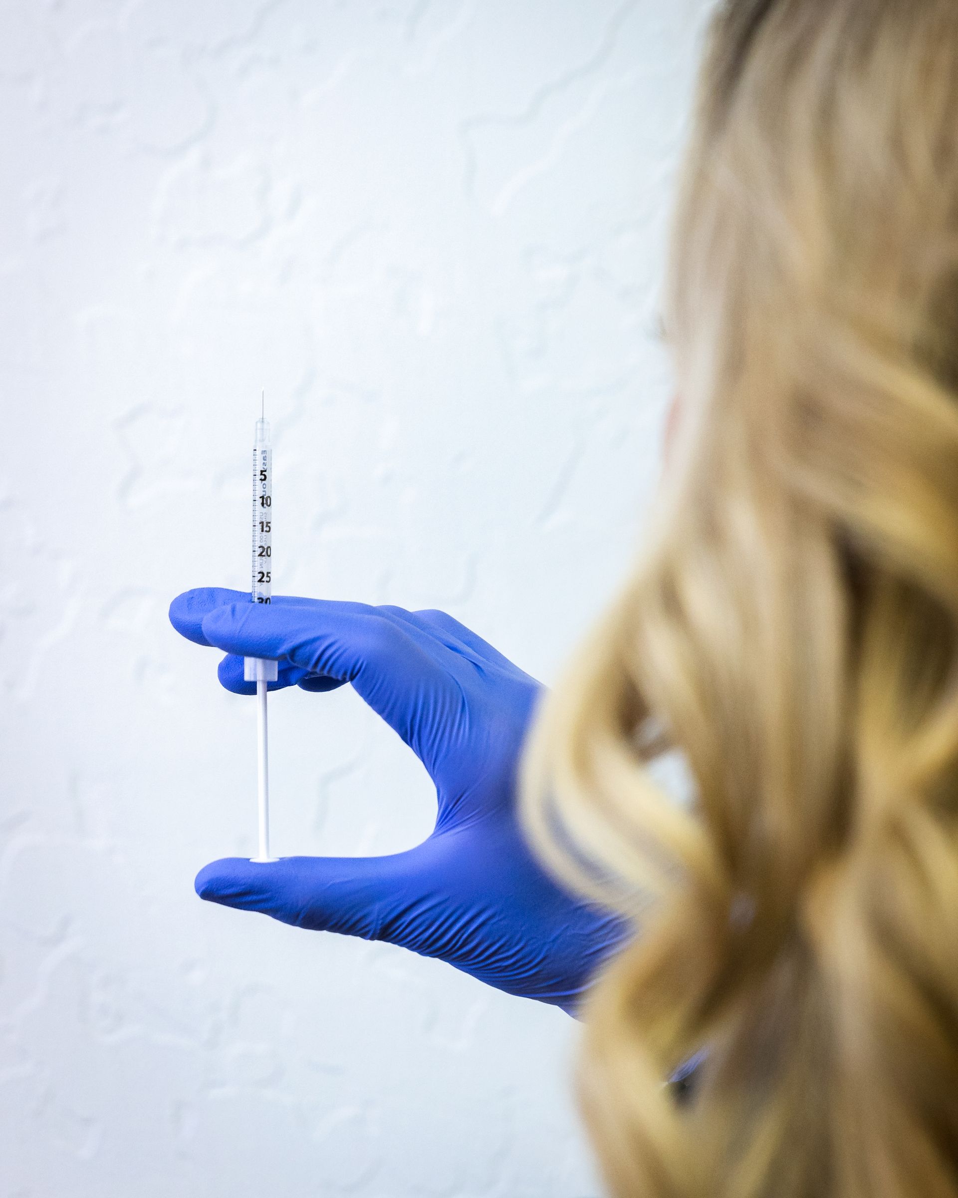Blue-gloved hand holding a clear test tube against a plain white wall