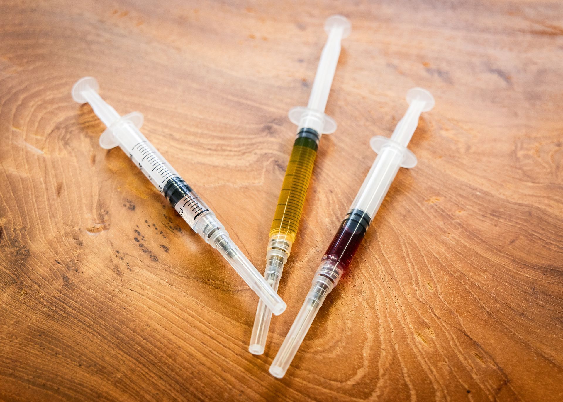 Three syringes with colored liquids on a wooden surface