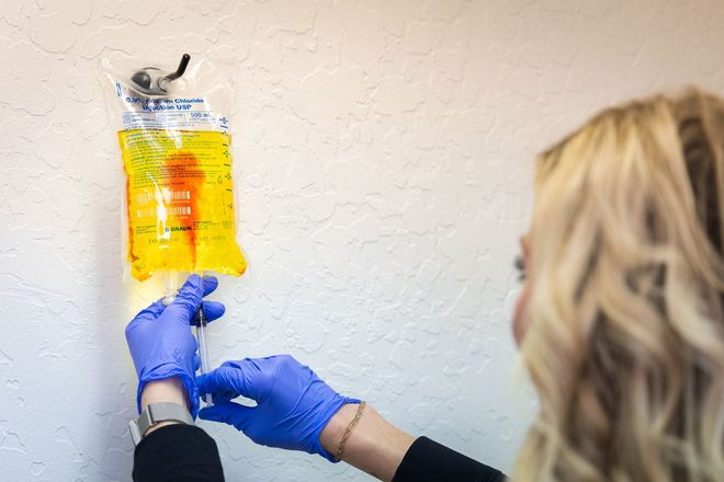 Gloved hands hang a yellow IV fluid bag on a wall hook