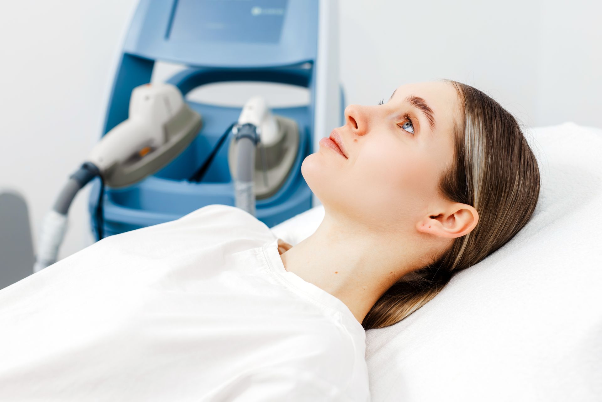 Woman receiving red-light treatment on her neck while reclined, with a handheld device pressed to her skin.
