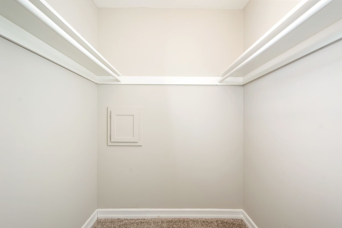 an empty walk in closet with white shelves and a window .