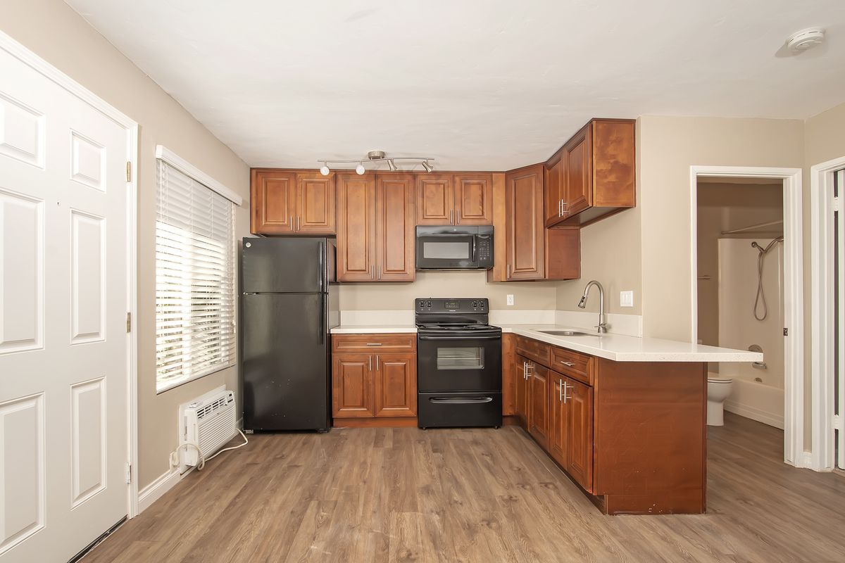 an empty kitchen with wooden cabinets and a black refrigerator .