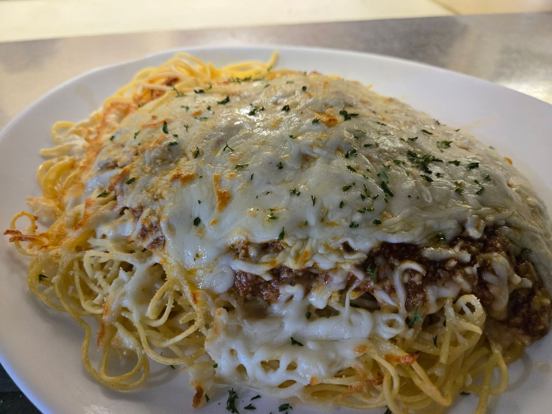 Une assiette de spaghettis nappée d'une riche sauce à la viande, de fromage blanc fondu et d'un peu d'herbes vertes.