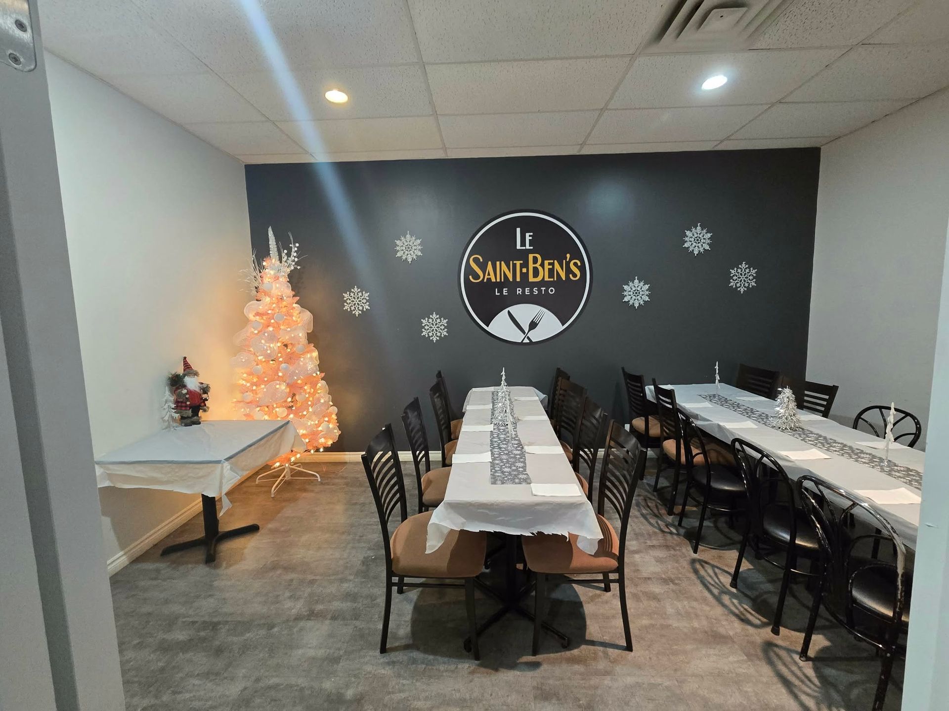 Une salle à manger avec un mur d'accent gris orné du logo de Saint-Ben, entourée de tables, de chaises et d'un arbre blanc.