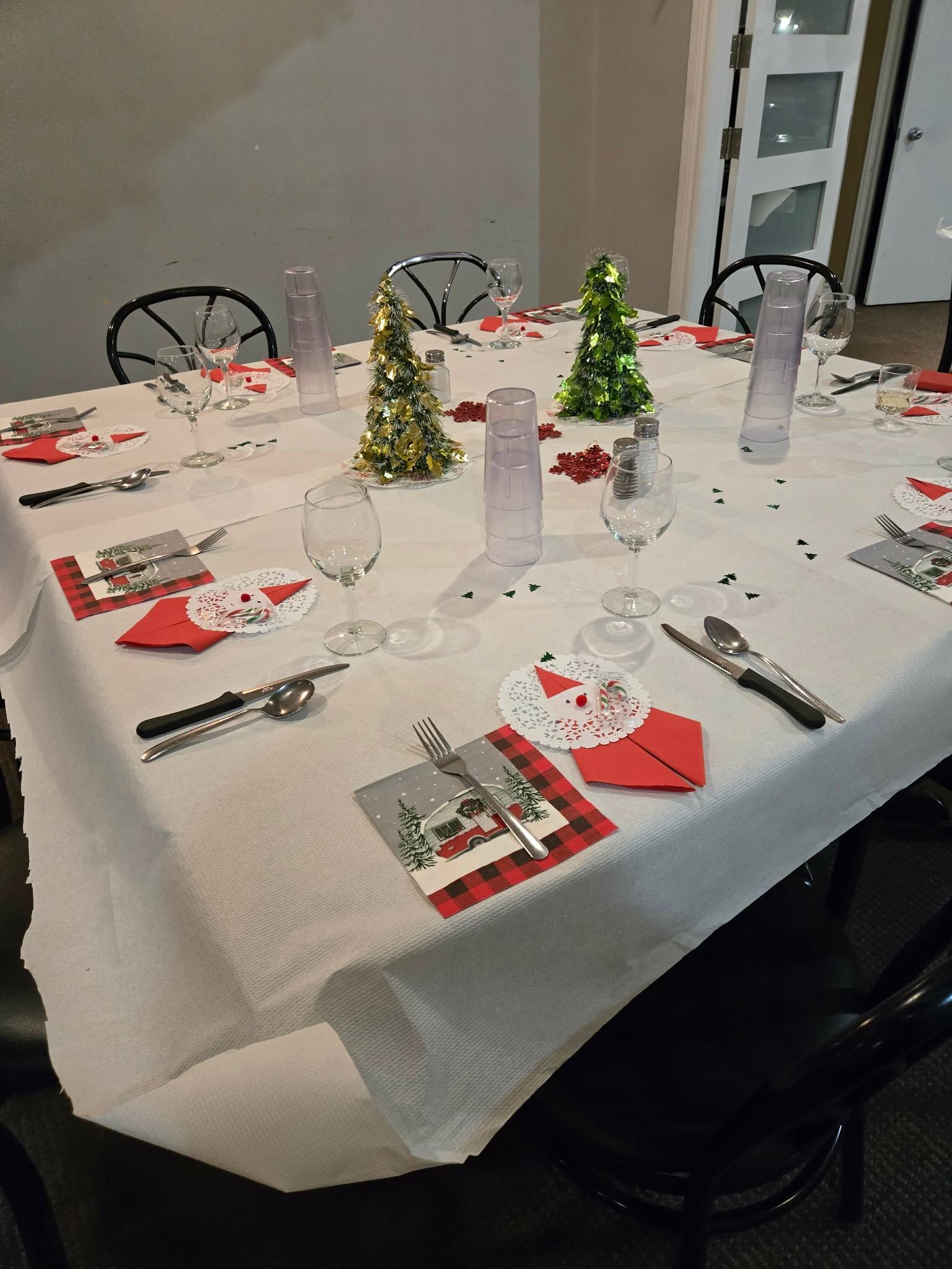 Une table dressée pour un dîner de fête avec des couverts rouges et blancs, des petits sapins de Noël en guirlandes et des verres à pied.