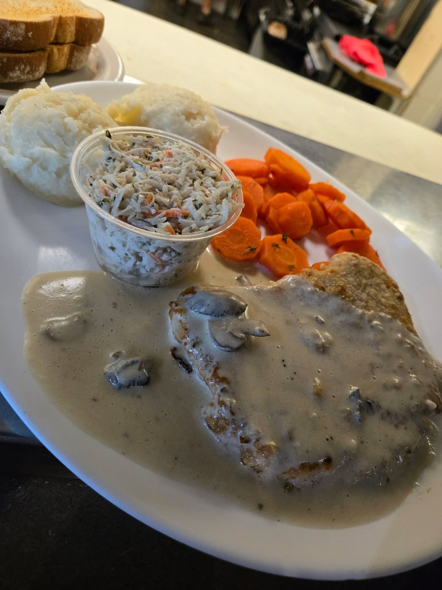 Une assiette composée d'un steak pané nappé de sauce, de purée de pommes de terre, de carottes cuites en tranches et d'une salade de chou.