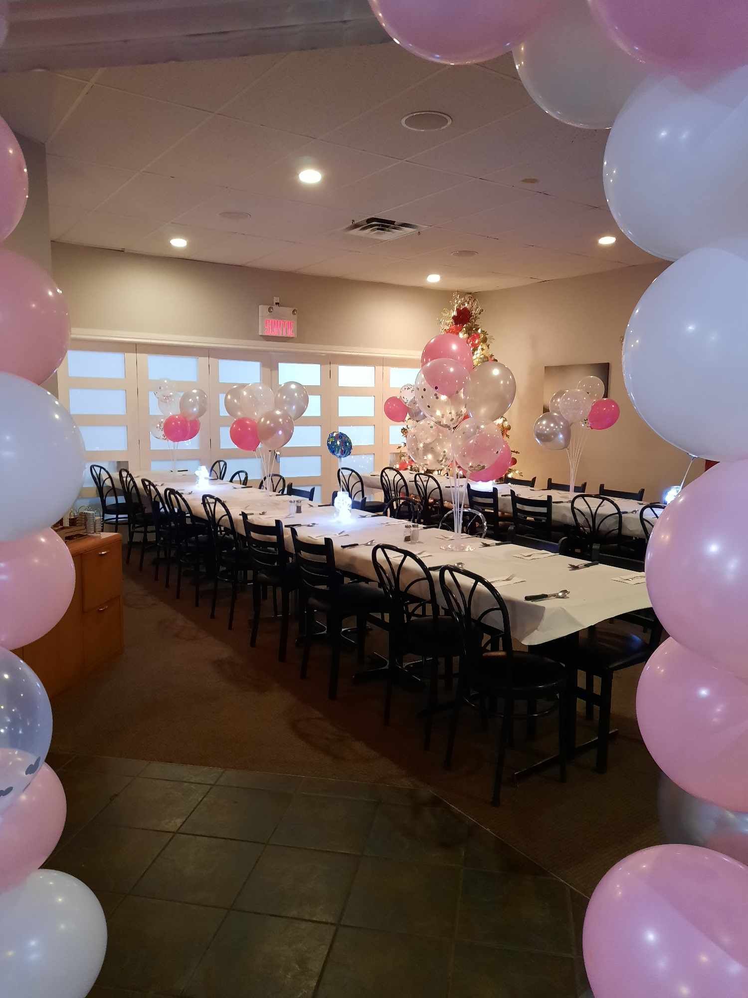 Une longue table dressée pour un événement formel dans une salle décorée d'arches et de grappes de ballons blancs et roses.