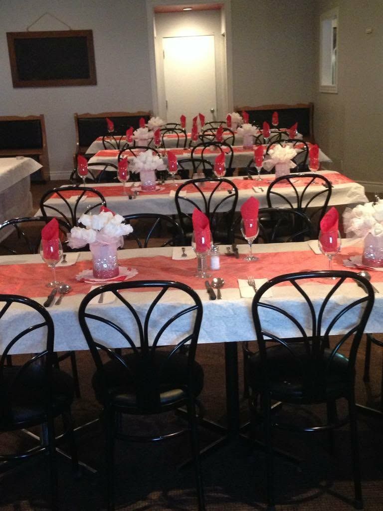 Tables dressées pour un événement formel avec nappes blanches, chemins de table roses, chaises noires et centres de table floraux.