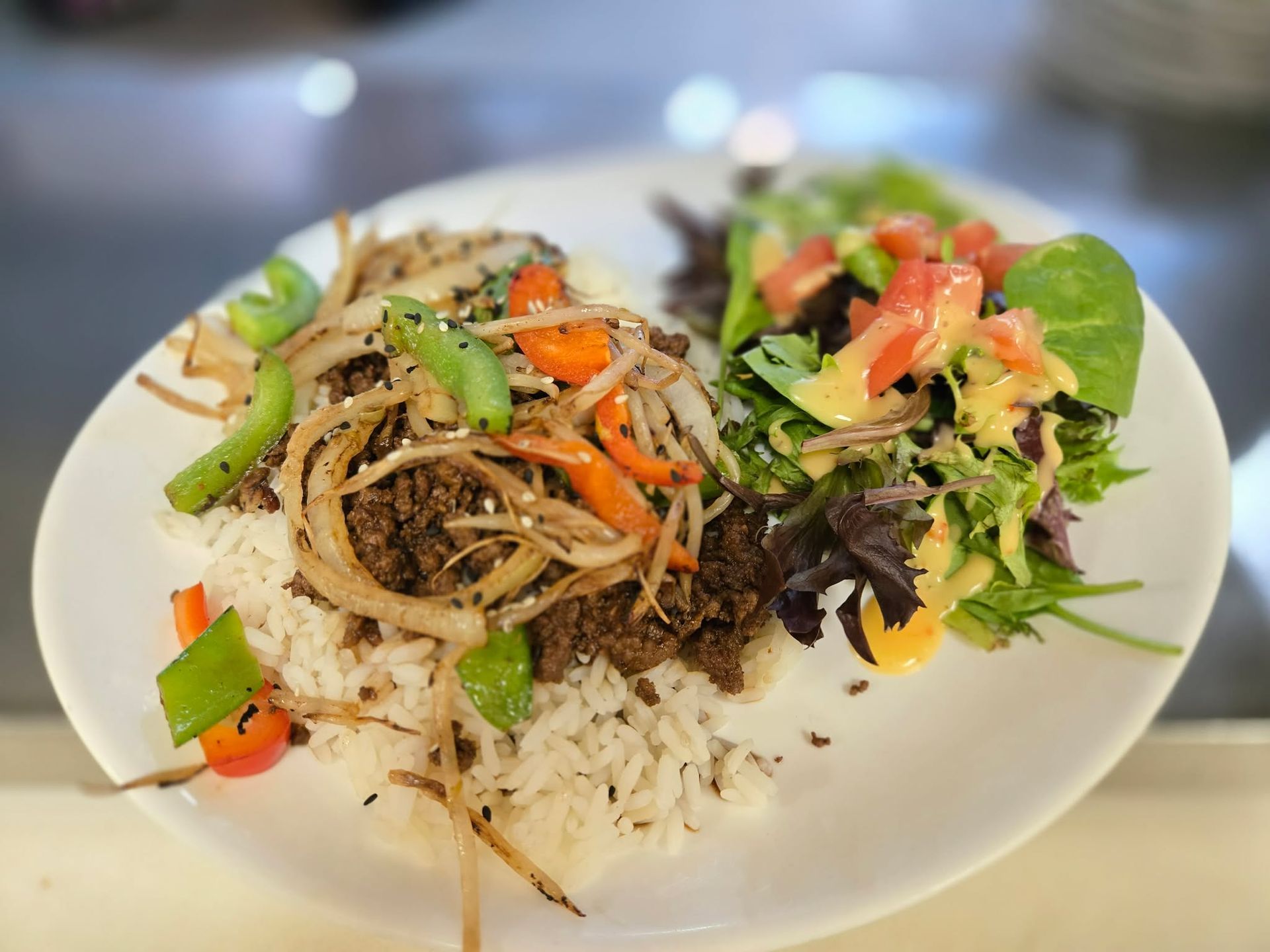 Une assiette de viande sautée aux oignons et aux poivrons, servie sur du riz blanc et accompagnée d'une salade verte composée.