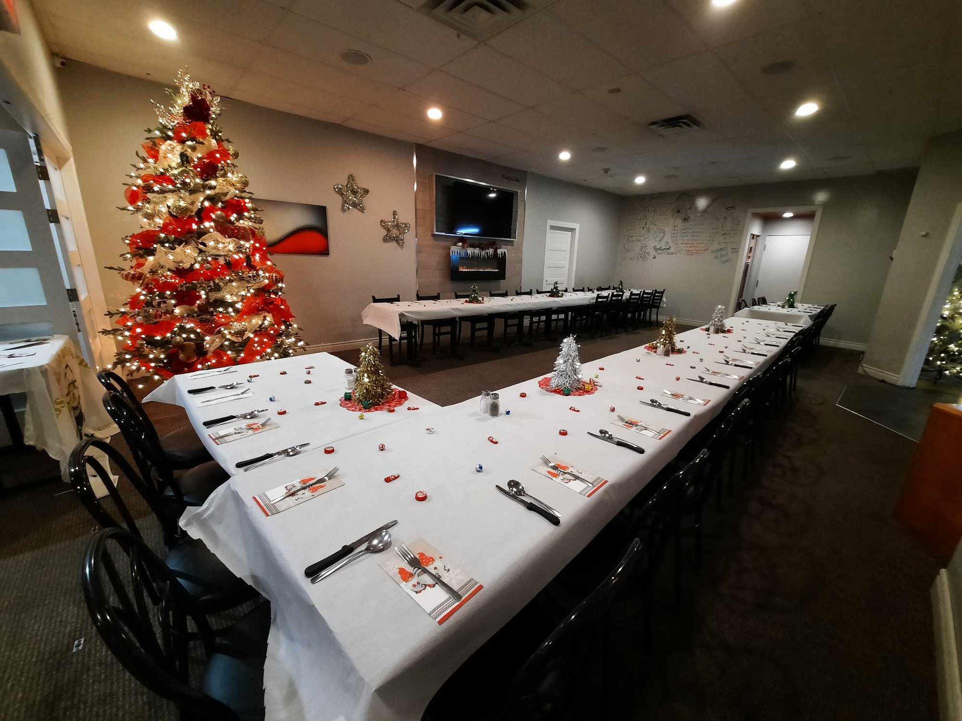 Une salle de banquet dressée pour un repas de fête, avec de longues tables disposées en forme de U, des nappes blanches et un sapin décoré.